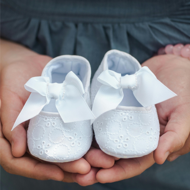 Hands holding white embroidered baby shoes with bows, baby gift, newborn accessories